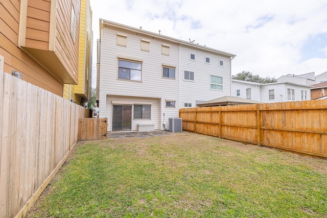 rear view of house featuring a fenced backyard, a yard, and central AC