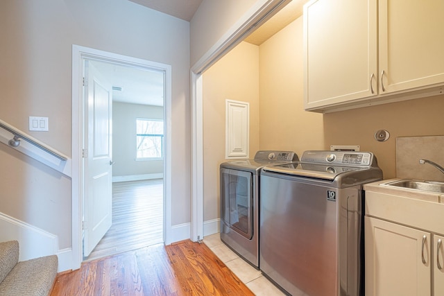clothes washing area with washing machine and clothes dryer, light wood finished floors, a sink, baseboards, and cabinet space