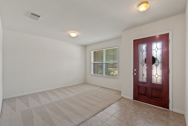 foyer with light tile patterned floors, baseboards, visible vents, and light colored carpet