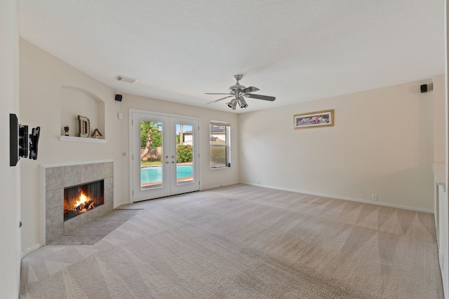 unfurnished living room with a ceiling fan, french doors, a tile fireplace, light colored carpet, and visible vents