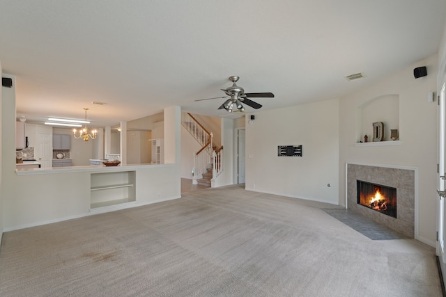 unfurnished living room featuring light carpet, visible vents, ceiling fan with notable chandelier, stairs, and a tile fireplace