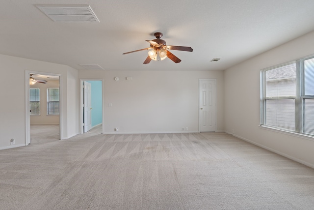 empty room with light carpet, a ceiling fan, visible vents, and baseboards