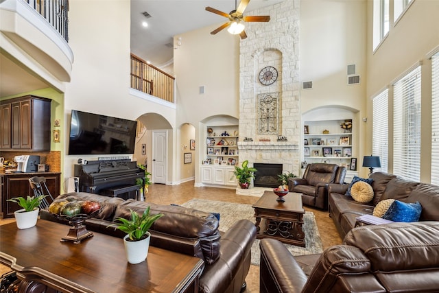 living area featuring visible vents, built in features, a ceiling fan, a high ceiling, and a stone fireplace