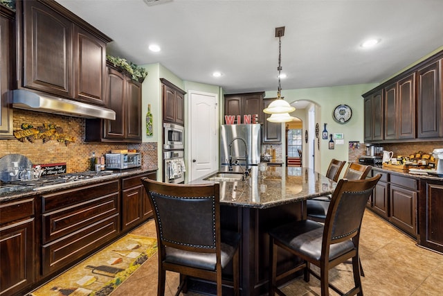 kitchen featuring under cabinet range hood, stainless steel appliances, a sink, arched walkways, and tasteful backsplash