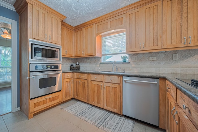 kitchen with stainless steel appliances, a sink, backsplash, light tile patterned floors, and crown molding