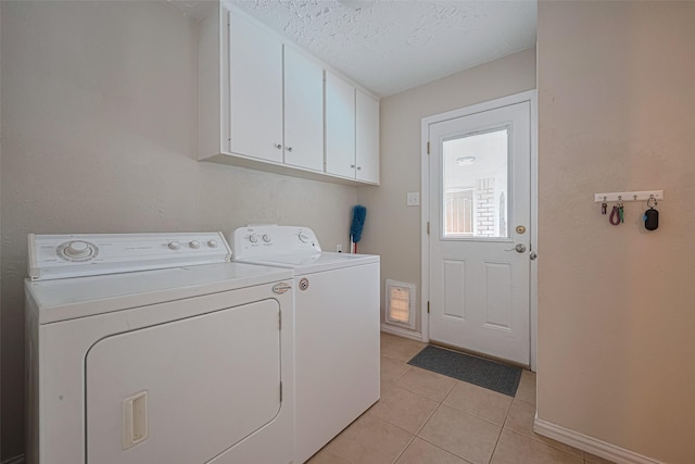 washroom featuring washer and dryer, cabinet space, light tile patterned floors, baseboards, and a textured ceiling