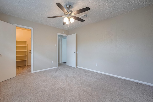 unfurnished bedroom with carpet floors, a spacious closet, baseboards, a textured ceiling, and a ceiling fan