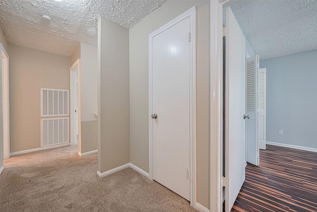 hall featuring a textured ceiling, carpet floors, and baseboards