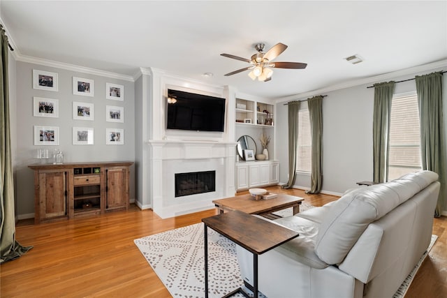living area with light wood-type flooring, visible vents, ceiling fan, a fireplace, and ornamental molding