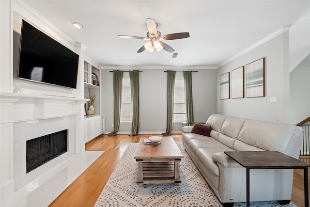 living area with visible vents, a premium fireplace, light wood-style floors, crown molding, and ceiling fan
