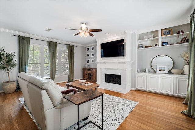 living room featuring a fireplace with flush hearth, light wood-style flooring, visible vents, ceiling fan, and ornamental molding