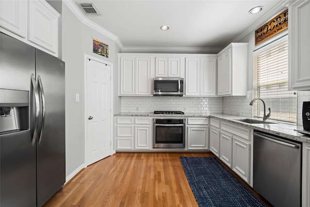 kitchen featuring a sink, stainless steel appliances, crown molding, visible vents, and light wood-style flooring