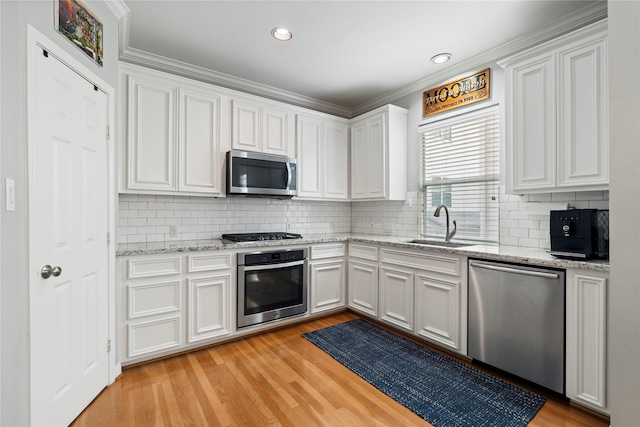 kitchen with stainless steel appliances, a sink, light wood-style floors, decorative backsplash, and white cabinetry