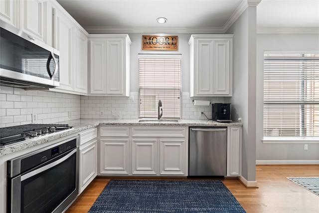 kitchen with a sink, decorative backsplash, light wood-style floors, white cabinets, and appliances with stainless steel finishes