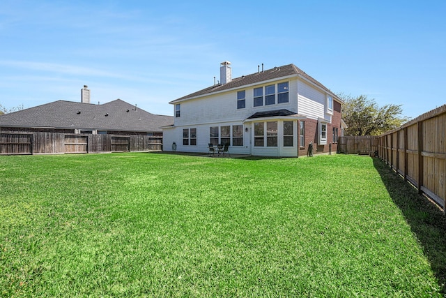 rear view of house featuring a fenced backyard, a lawn, and a chimney