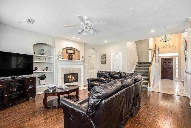 living room with built in features, a fireplace, stairs, wood-type flooring, and ceiling fan with notable chandelier