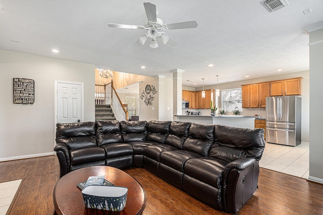 living room with light wood finished floors, visible vents, stairs, and ceiling fan