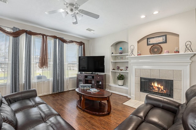 living room featuring built in features, ceiling fan, visible vents, and wood finished floors