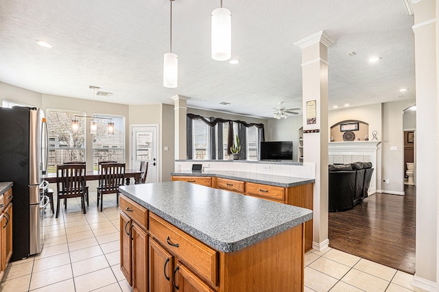 kitchen featuring freestanding refrigerator, decorative columns, a ceiling fan, a center island, and open floor plan
