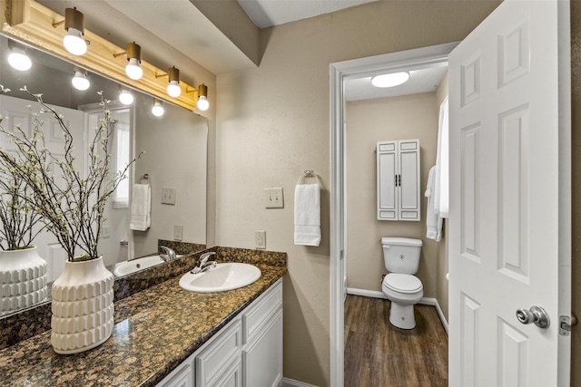 bathroom with toilet, vanity, wood finished floors, and baseboards