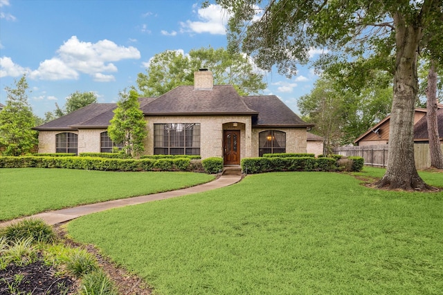 french provincial home with fence, a chimney, a front yard, and brick siding