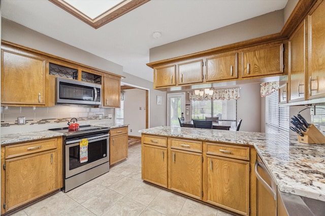 kitchen with brown cabinetry, a peninsula, light tile patterned floors, appliances with stainless steel finishes, and backsplash