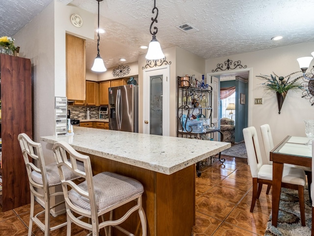 1814 Cliffdale Dr, Missouri City, TX 77489 - kitchen with visible vents, a peninsula, brown cabinetry, a textured ceiling, and stainless steel refrigerator with ice dispenser