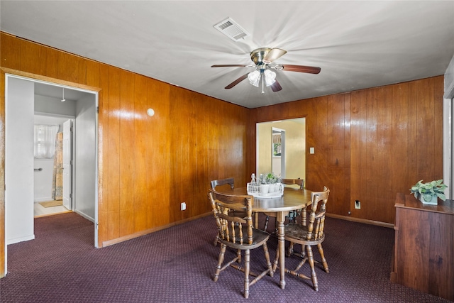 dining room with wood walls, a ceiling fan, visible vents, and carpet flooring