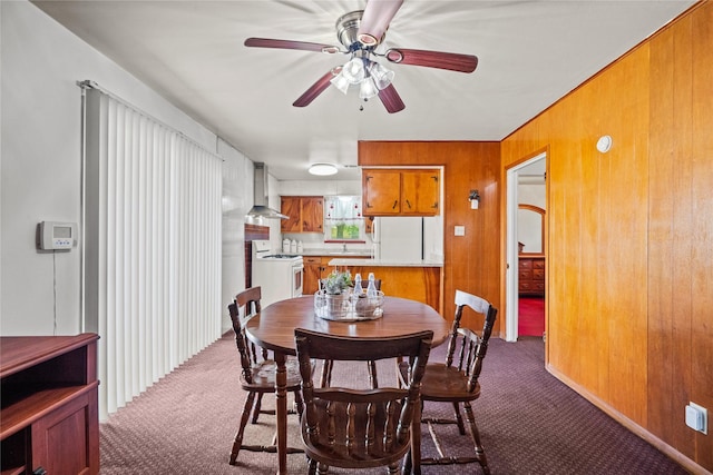 dining space with dark carpet, ceiling fan, and wood walls