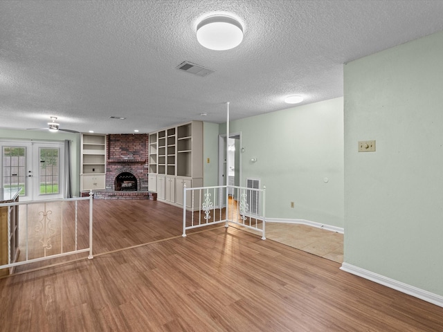 unfurnished living room featuring ceiling fan, a textured ceiling, visible vents, and wood finished floors