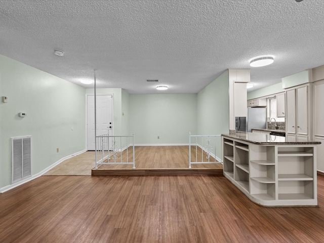 unfurnished living room featuring visible vents, a sink, baseboards, and wood finished floors