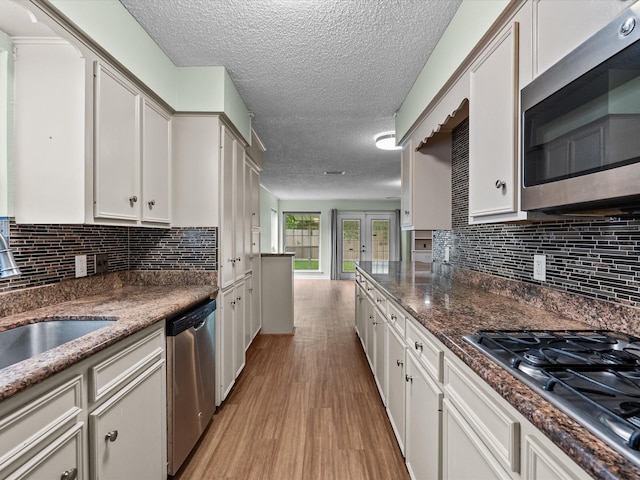 kitchen featuring backsplash, a textured ceiling, a sink, light wood finished floors, and stainless steel appliances