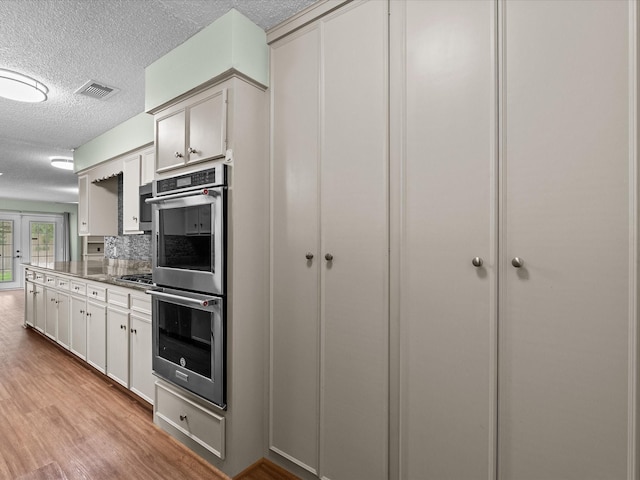 kitchen featuring stainless steel double oven, a textured ceiling, white cabinetry, light wood-type flooring, and visible vents