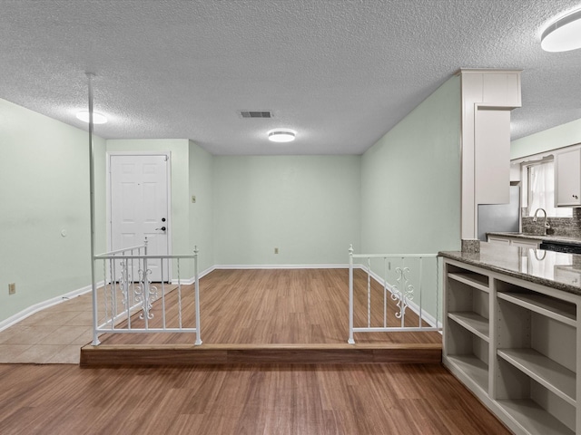 interior space featuring a textured ceiling, baseboards, wood finished floors, and visible vents