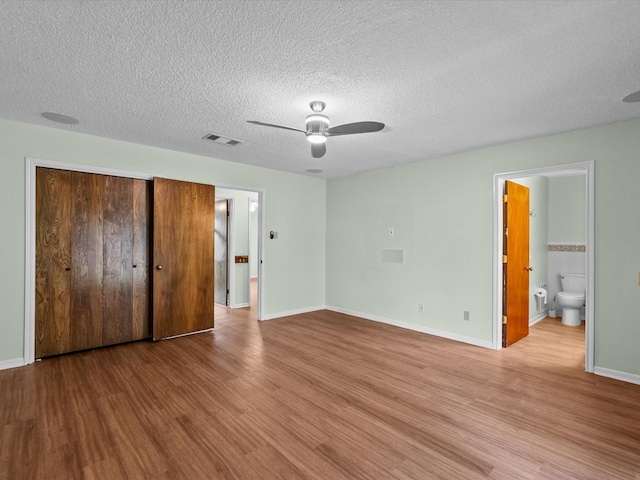 unfurnished bedroom with a textured ceiling, visible vents, wood finished floors, baseboards, and a closet