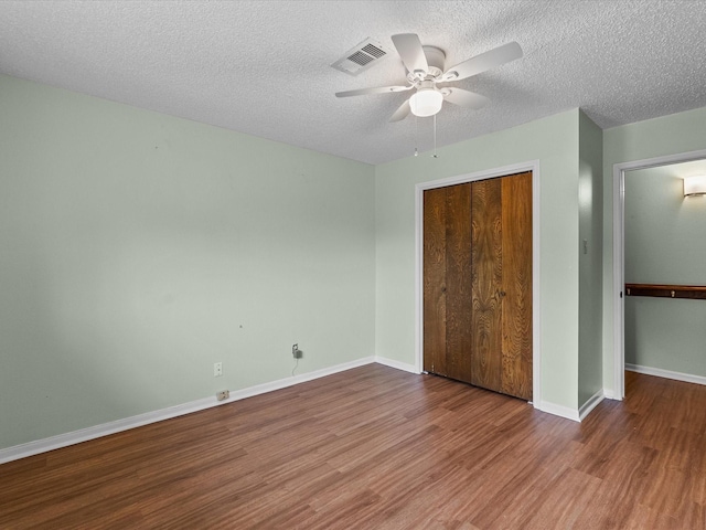 unfurnished bedroom featuring a textured ceiling, visible vents, wood finished floors, and a closet