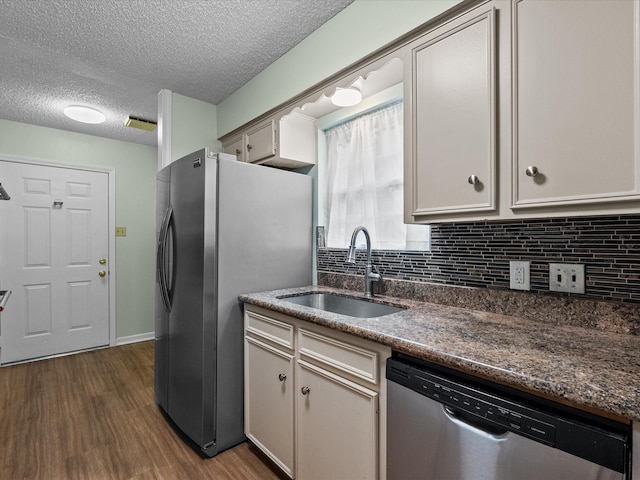 kitchen with appliances with stainless steel finishes, tasteful backsplash, a sink, and dark wood finished floors