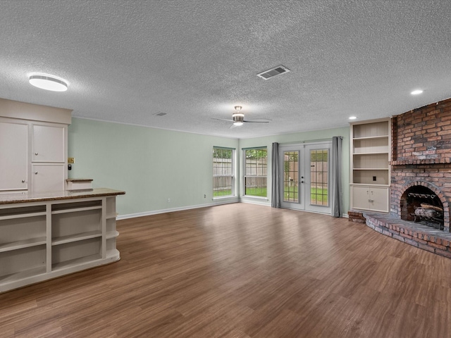 unfurnished living room with a ceiling fan, a textured ceiling, a brick fireplace, wood finished floors, and baseboards