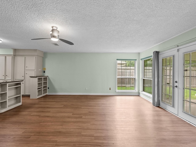 unfurnished living room featuring ceiling fan, a textured ceiling, french doors, baseboards, and wood finished floors
