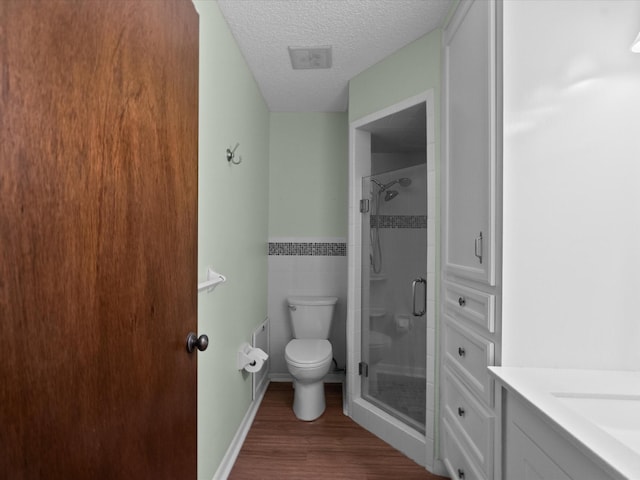 bathroom with a textured ceiling, visible vents, a shower stall, wood finished floors, and toilet