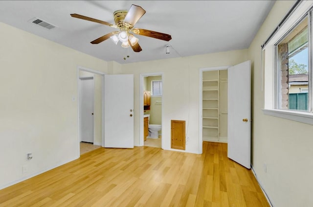 unfurnished bedroom featuring a closet, a spacious closet, light wood finished floors, ensuite bath, and visible vents