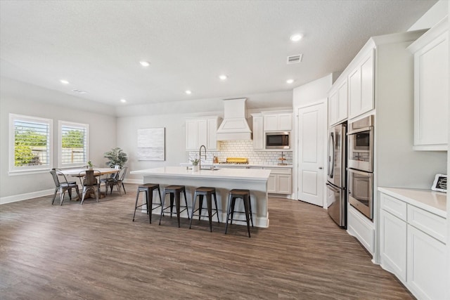 kitchen with a kitchen breakfast bar, a center island with sink, visible vents, custom exhaust hood, and appliances with stainless steel finishes