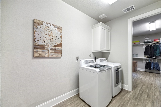 washroom with baseboards, visible vents, light wood-style floors, cabinet space, and washer and dryer