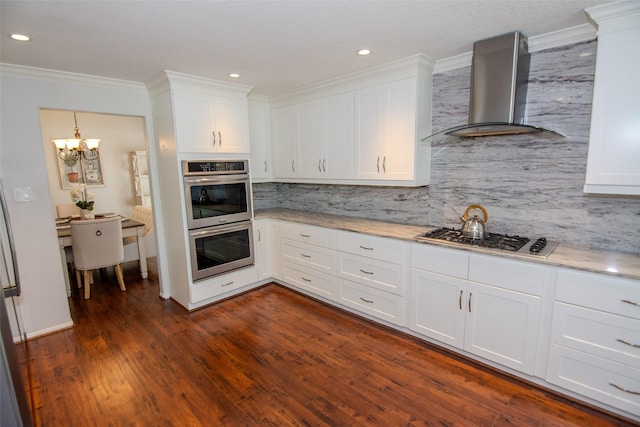 kitchen with white cabinets, wall chimney exhaust hood, tasteful backsplash, appliances with stainless steel finishes, and a notable chandelier