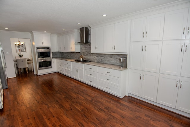 kitchen with white cabinets, an inviting chandelier, wall chimney range hood, decorative backsplash, and appliances with stainless steel finishes