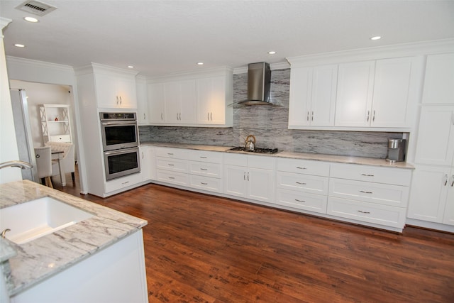 kitchen with white cabinets, stainless steel appliances, a sink, wall chimney exhaust hood, and crown molding