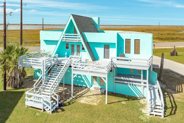 exterior space with a lawn, a deck, stairs, and a shingled roof
