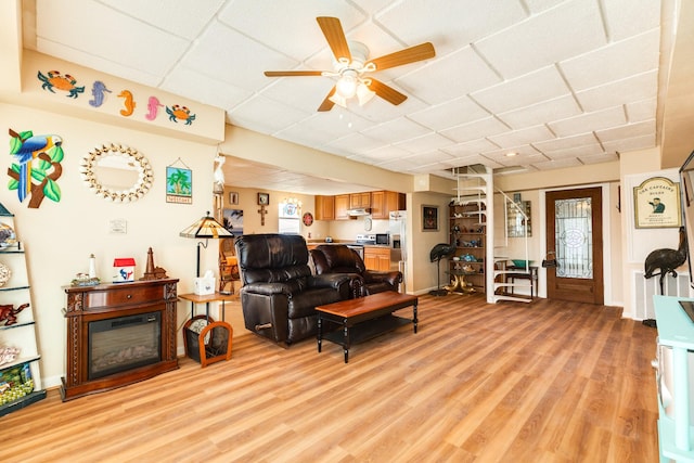 living area featuring a ceiling fan, a drop ceiling, and light wood-style flooring
