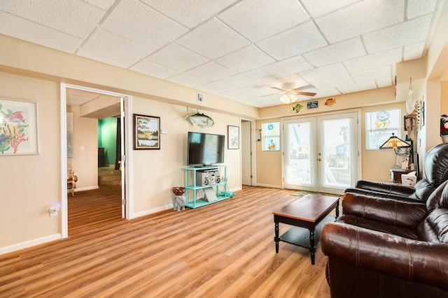living room featuring a ceiling fan, a drop ceiling, french doors, light wood finished floors, and baseboards