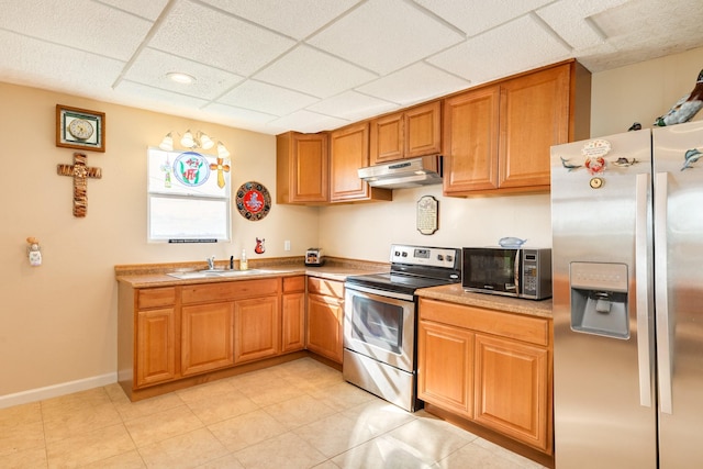 kitchen with a sink, a drop ceiling, brown cabinetry, under cabinet range hood, and appliances with stainless steel finishes
